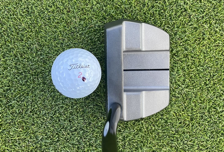 Close-up of a putter head ready to hit a white golf ball.