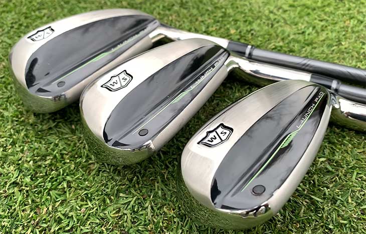 Close-up of three golfing irons sitting on lush green grass.