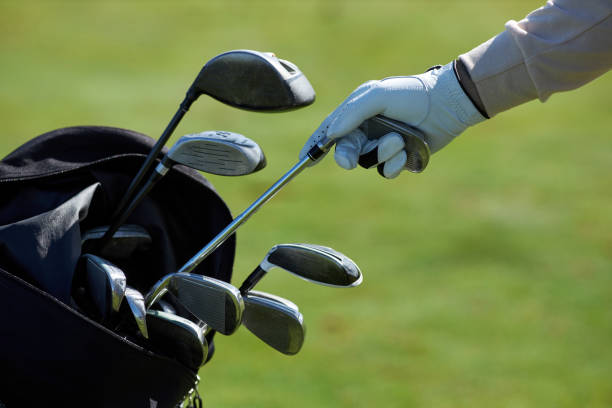 Closeup of unrecognizable golf player choosing club and taking out of golf bag against green grass background