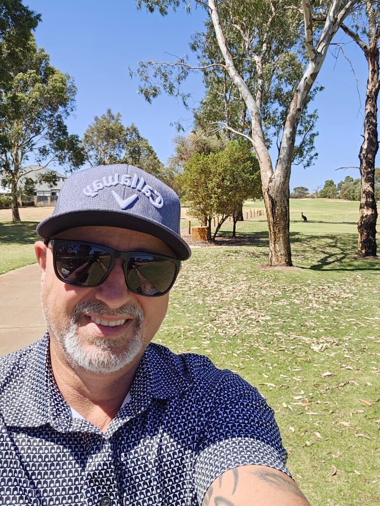 A close up of a man on a golf course with a blue Callaway golf cap and blue dotted shirt